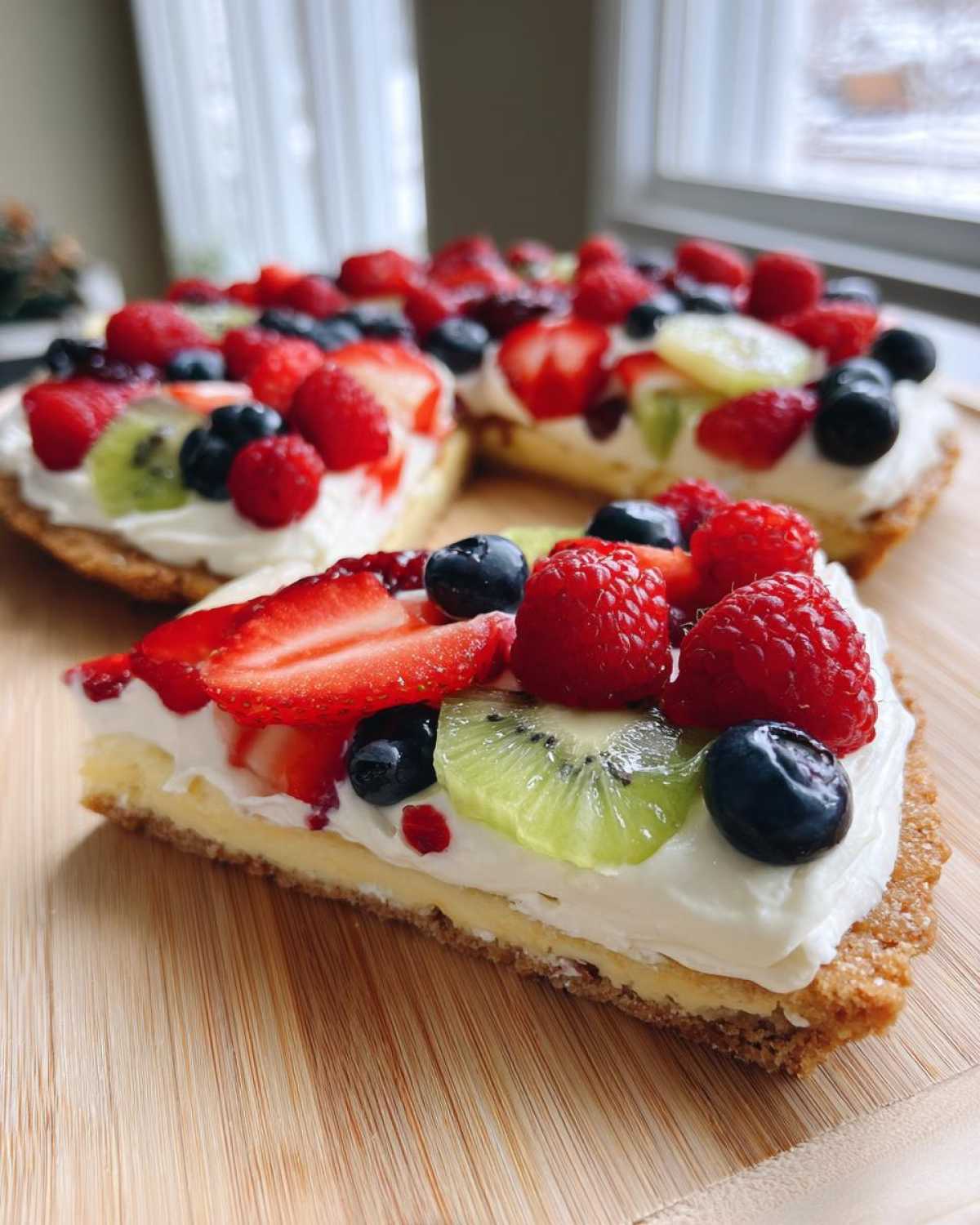 A slice of fruit pizza sugar cookie topped with fresh berries, kiwi, and a creamy frosting.