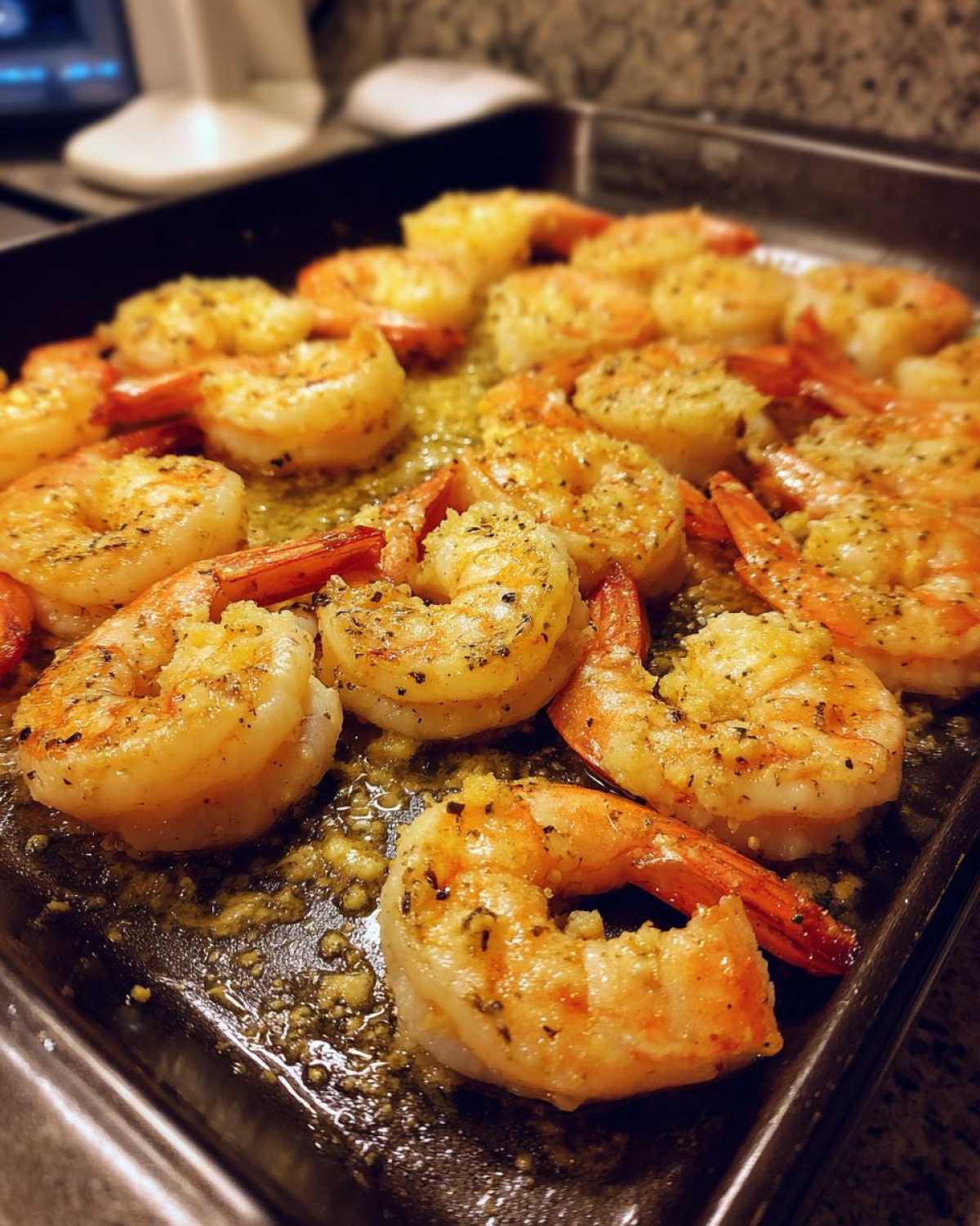 Close-up of Garlic Parmesan baked shrimp on a dark baking sheet, seasoned with herbs and spices.