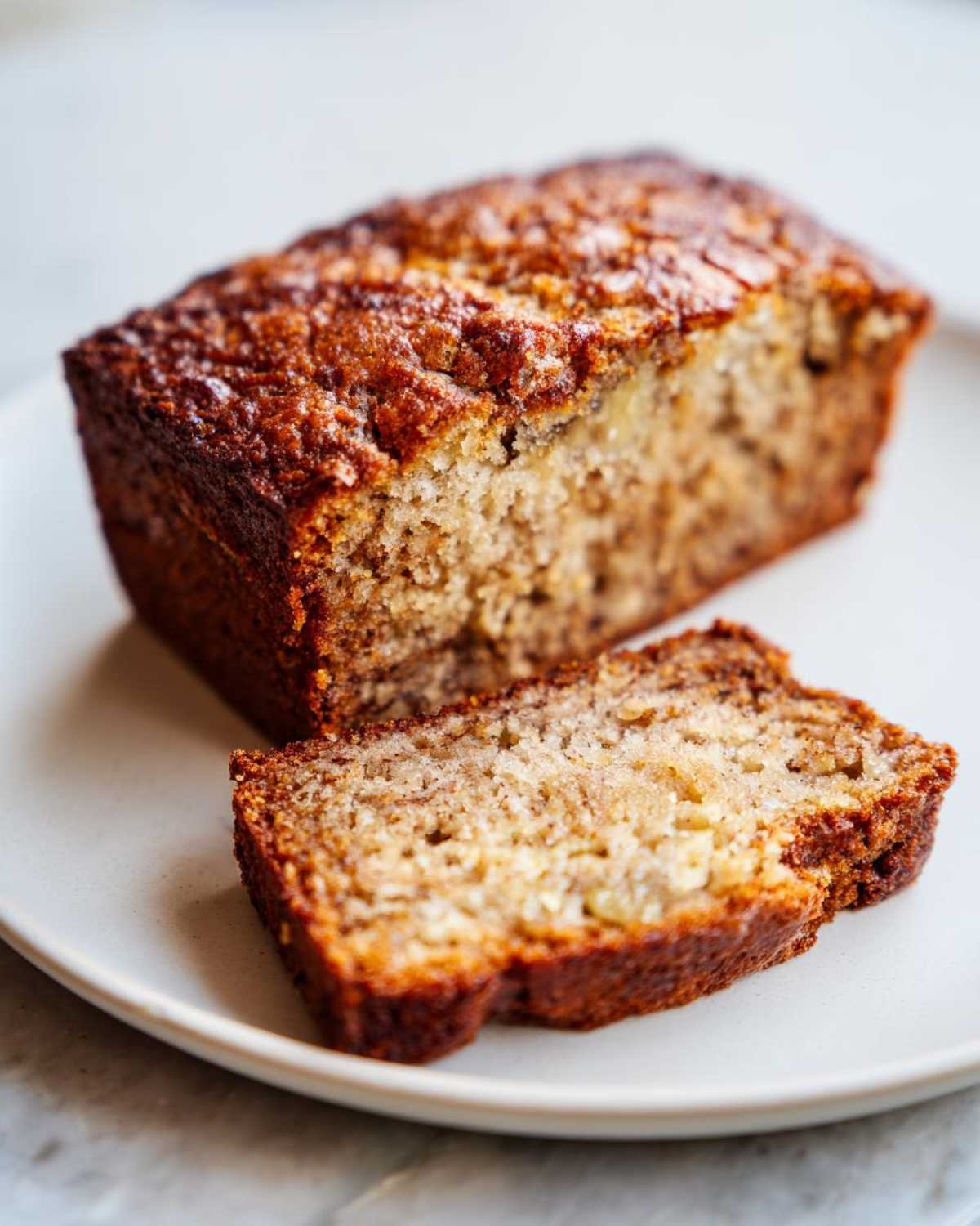 A loaf of high protein banana bread with a slice cut, displayed on a white plate.