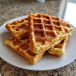 A stack of golden brown high protein waffles on a white plate, ready to eat.
