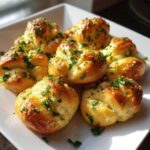 A plate of freshly baked homemade garlic knots, topped with garlic and parsley.