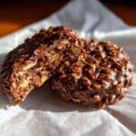 A close-up of no-bake chocolate oatmeal cookies, one broken in half to show the texture.