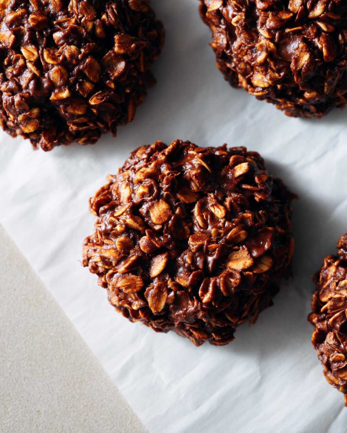 Close-up of several no-bake chocolate oatmeal cookies on parchment paper, showcasing their texture.
