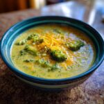 A bowl of creamy Panera broccoli cheddar soup copycat topped with broccoli florets and shredded cheddar cheese.