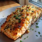 A delicious parmesan crusted baked salmon fillet on a plate, garnished with fresh herbs.