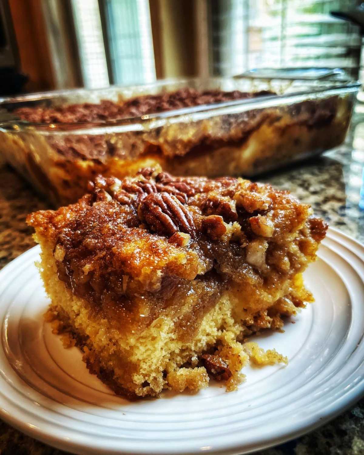 A slice of pecan pie dump cake on a white plate, topped with pecans and a gooey filling.