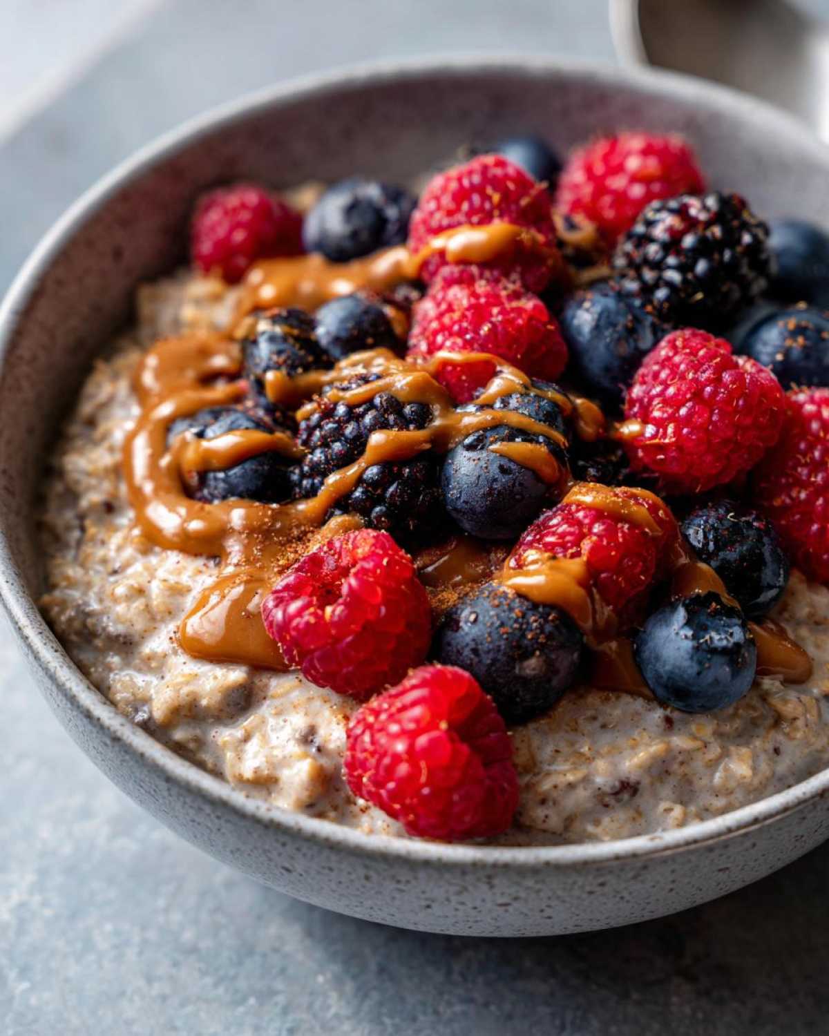 Bowl of protein oatmeal topped with fresh raspberries, blueberries, blackberries, and a drizzle of nut butter.