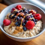 A tempting bowl of protein oatmeal topped with fresh raspberries, blueberries, blackberries, and a drizzle of nut butter.