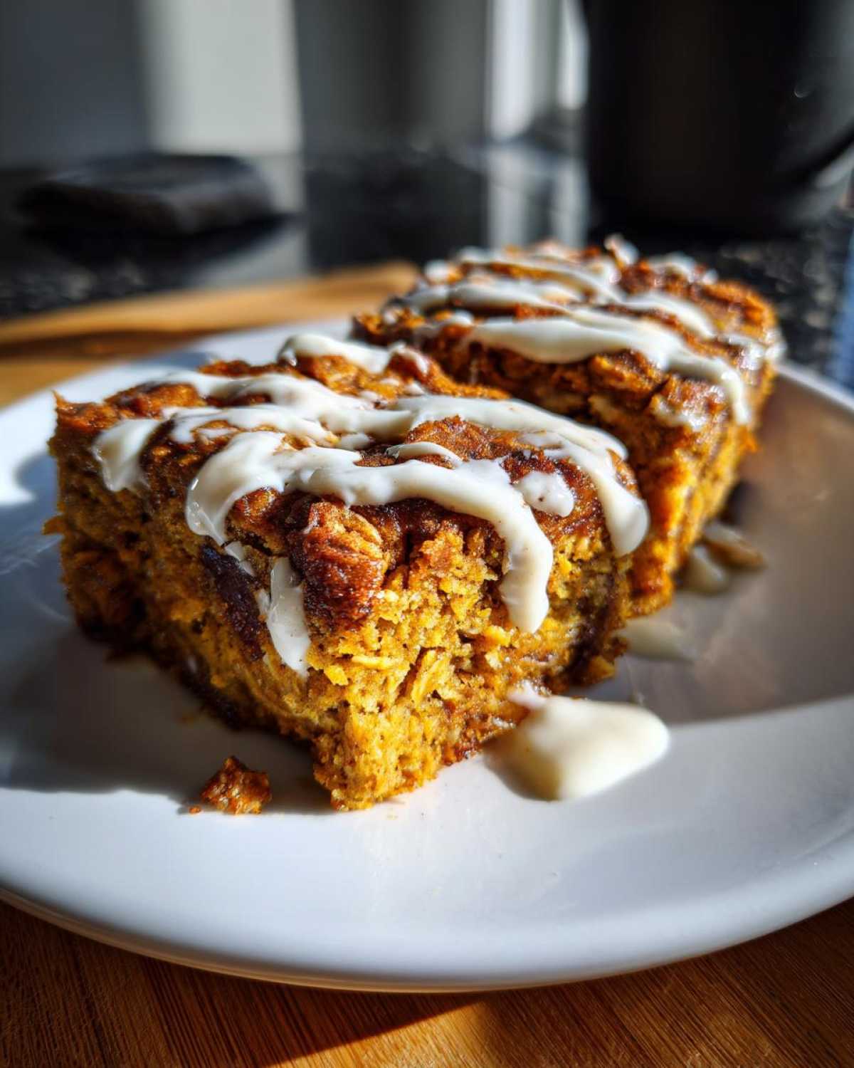 Two slices of pumpkin baked oatmeal on a white plate, drizzled with cream cheese frosting.