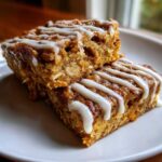Two squares of pumpkin baked oatmeal stacked on a plate, drizzled with a sweet white glaze.