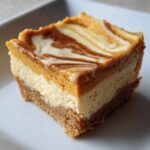 Close-up of a pumpkin cheesecake bar with a graham cracker crust and a swirl of pumpkin puree.