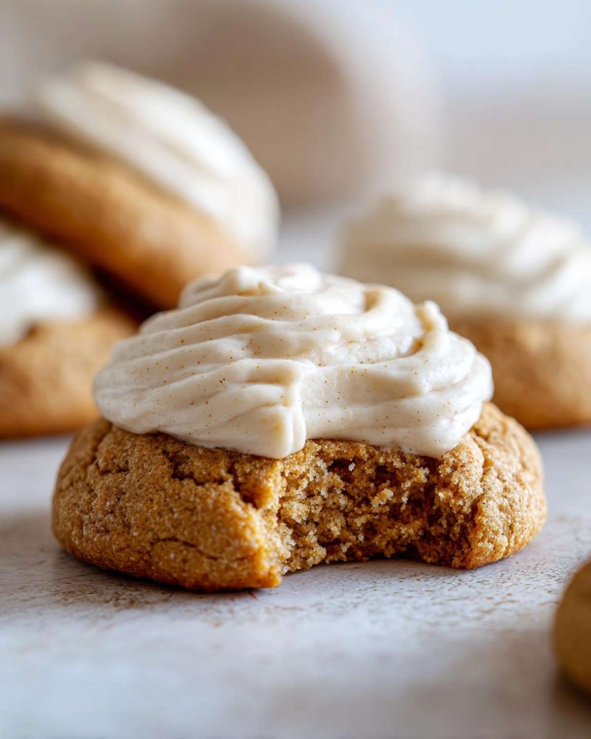 Close-up of a pumpkin cheesecake cookie with a bite taken out, topped with creamy frosting.