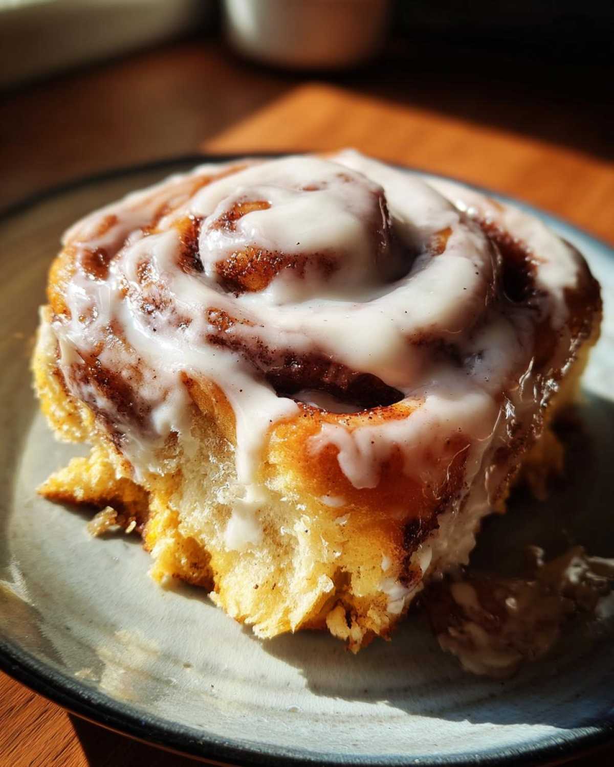 A single pumpkin cinnamon roll with icing on a plate, showcasing its swirl and texture.