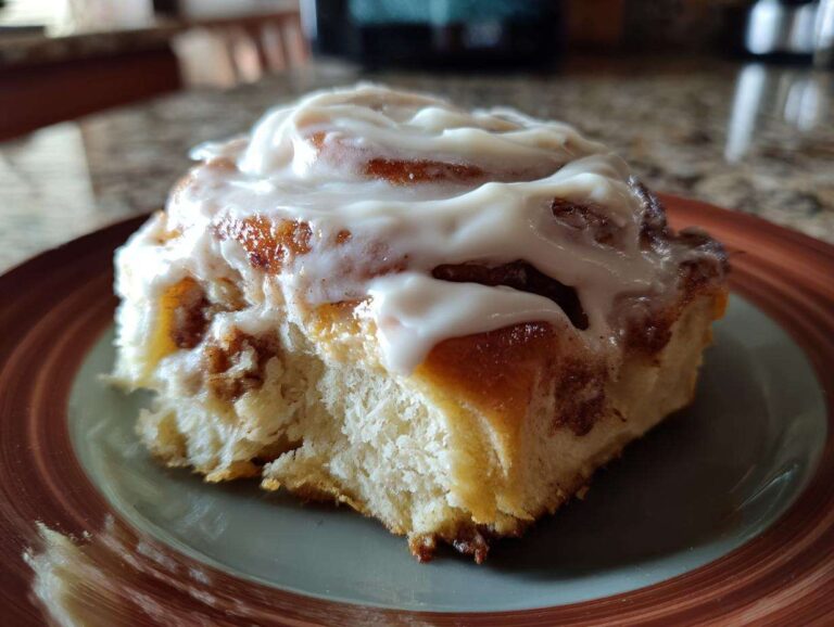A single pumpkin cinnamon roll topped with white icing, sitting on a brown and green plate.