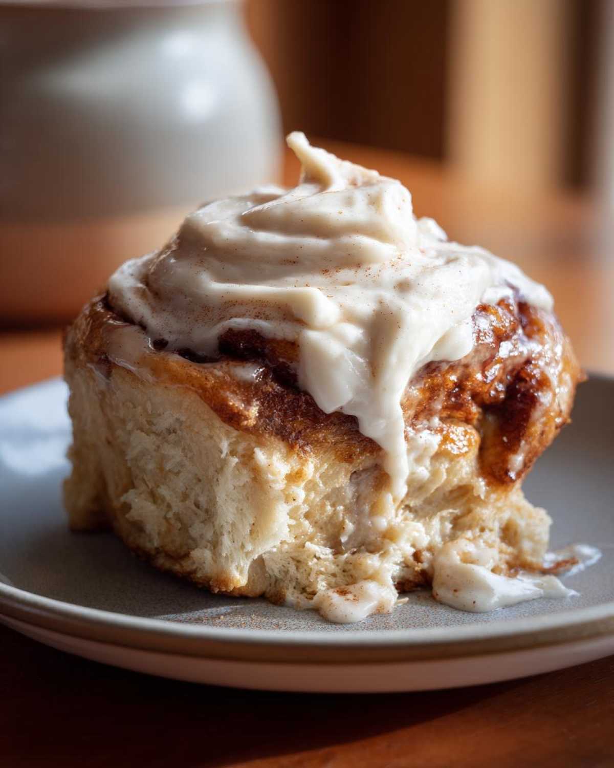 Close-up of a single pumpkin cinnamon roll with cream cheese frosting on a small plate.