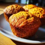 Four freshly baked pumpkin protein muffins arranged on a plate, showcasing their golden-brown color and texture.