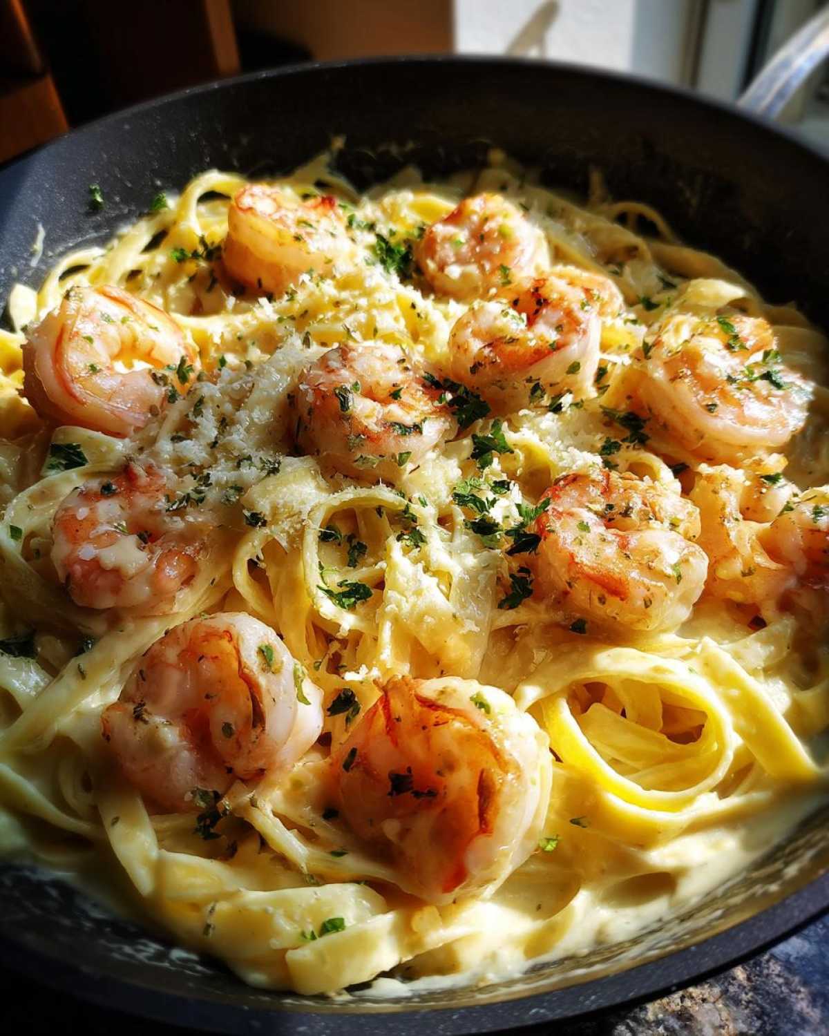 Close-up of Shrimp Alfredo pasta in a pan, topped with parmesan cheese and parsley.