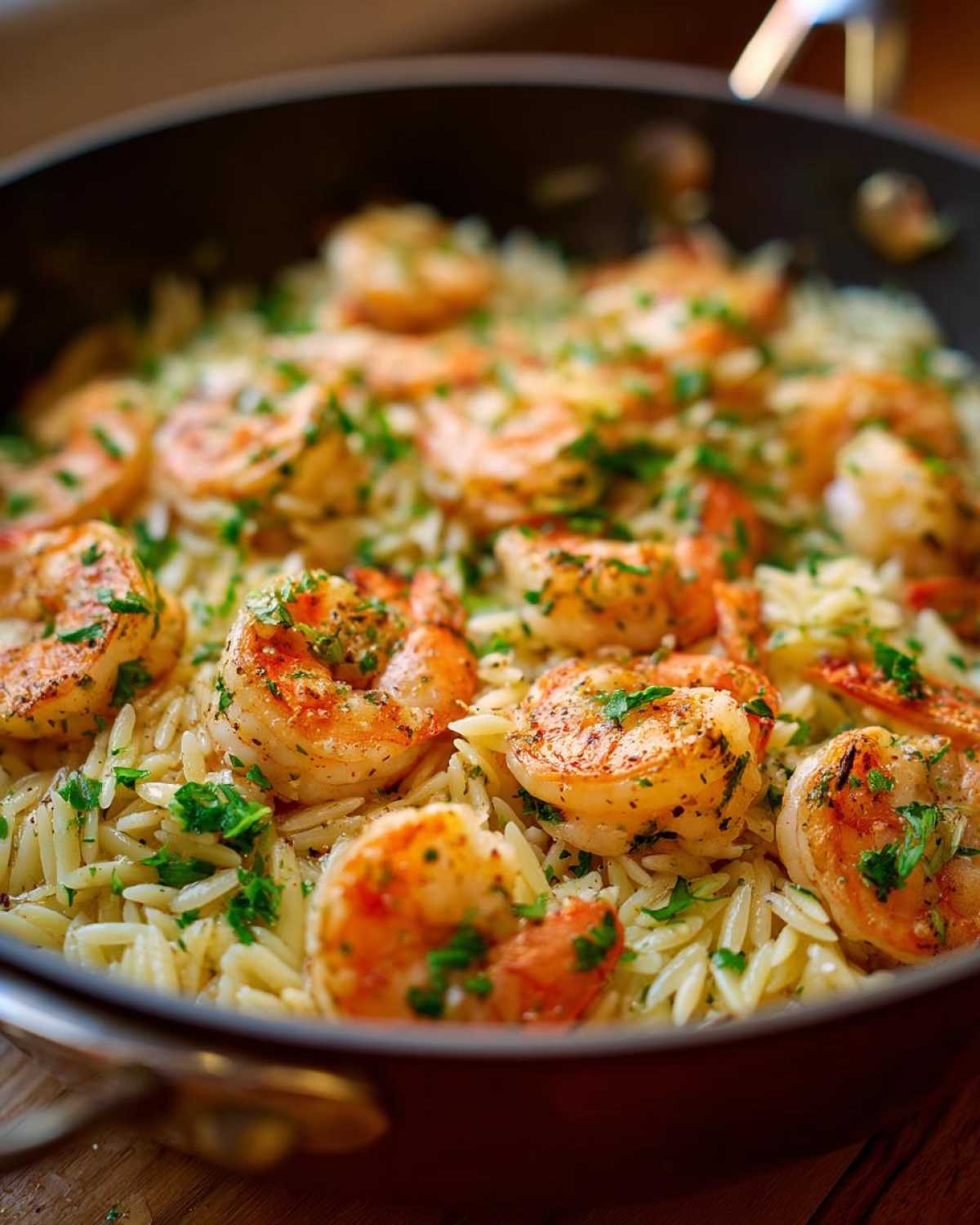 Close-up of shrimp orzo in lemon garlic sauce, cooked in a pan and garnished with parsley.