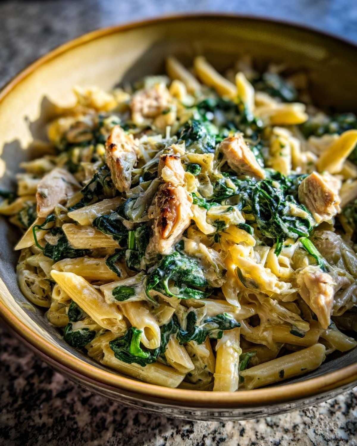 A bowl of creamy spinach artichoke pasta with penne, spinach, artichoke hearts, and chicken.