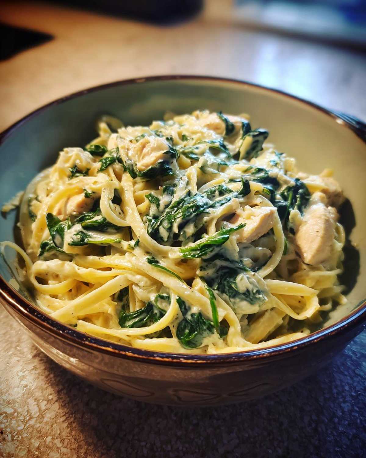 Bowl of creamy spinach artichoke pasta with fettuccine, spinach, artichoke hearts, and chicken.