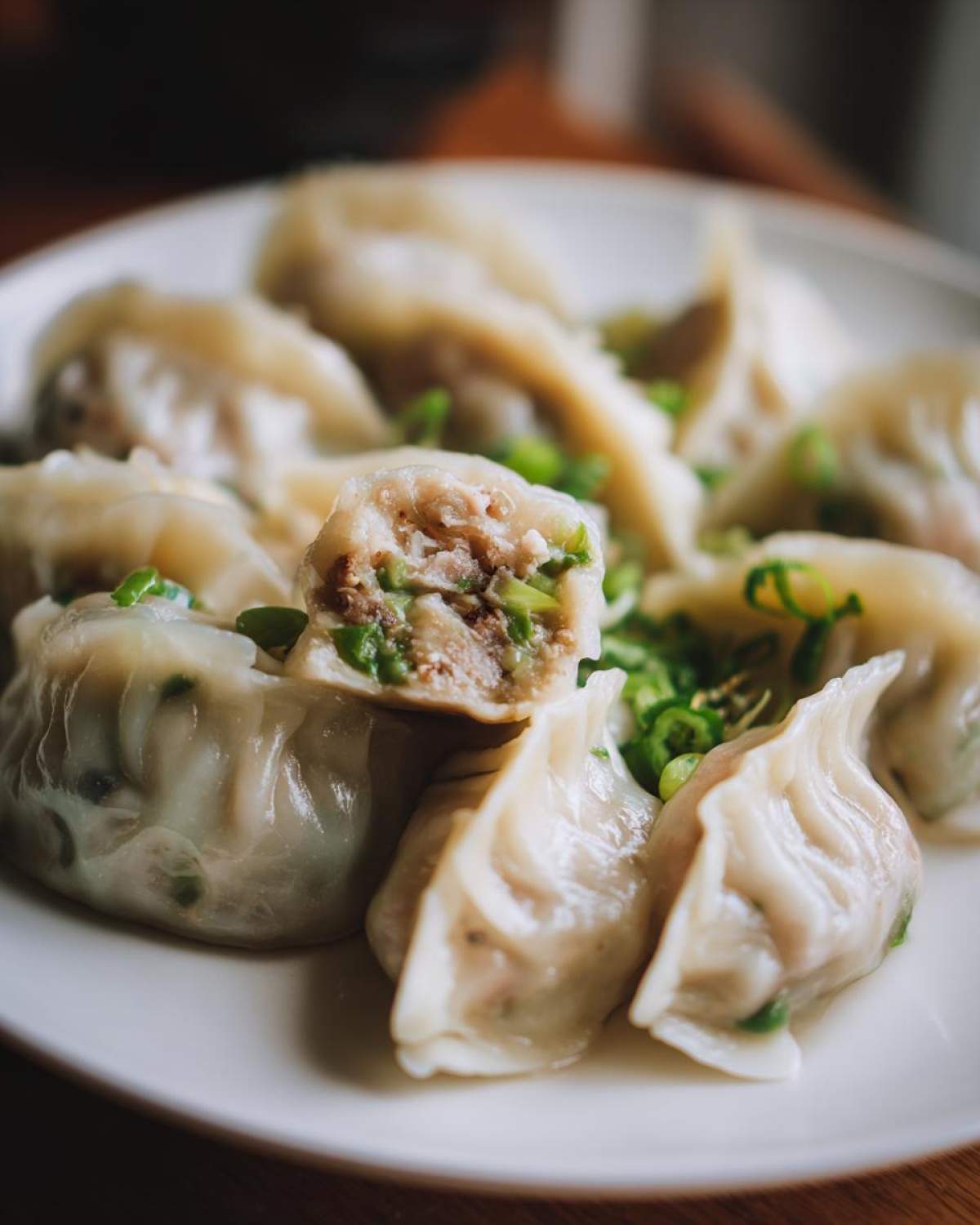 A plate of Traditional Chinese Dumplings, one cut open to show the filling, garnished with sliced green onions.
