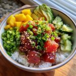 A vibrant Tuna Poke Bowl with rice, tuna, mango, avocado, cucumber, and green onions.