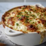 Close-up of creamy white lasagna soup in a white bowl, topped with melted cheese and parsley.