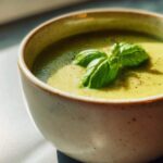 Bowl of creamy zucchini soup garnished with fresh basil leaves and black pepper.