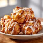 A stack of golden air fryer apple fritters drizzled with sweet white glaze on a plate.