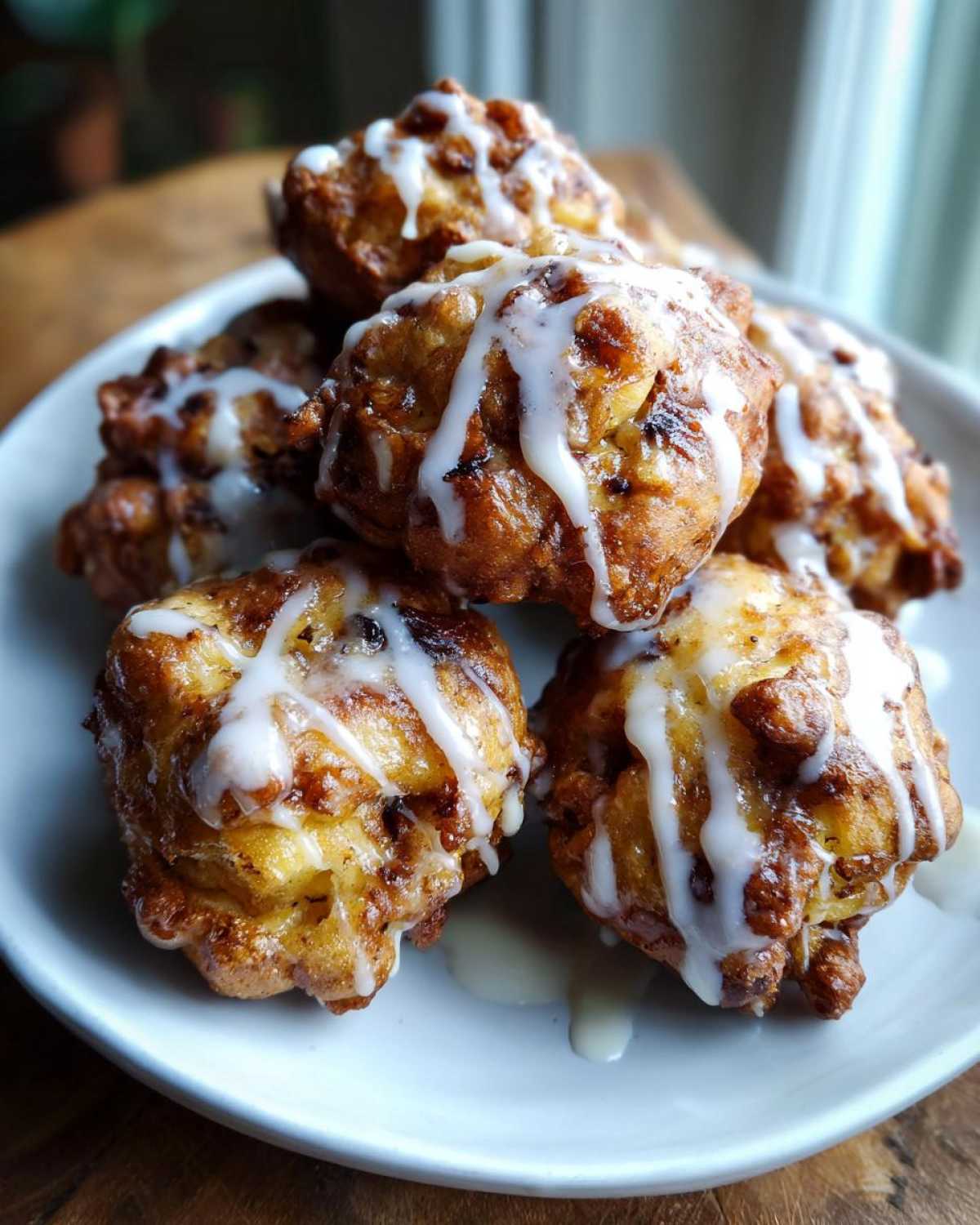 A stack of golden air fryer apple fritters drizzled with a sweet glaze on a white plate.