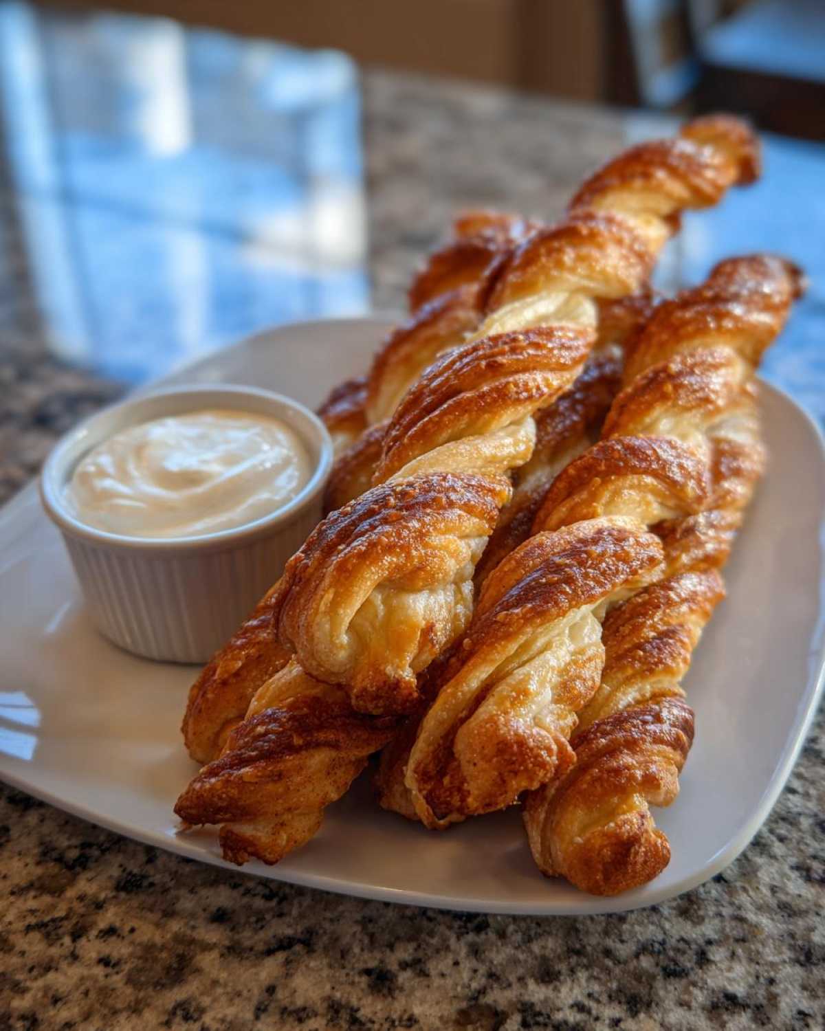 A plate of golden brown air fryer cinnamon twists served with a creamy dipping sauce.
