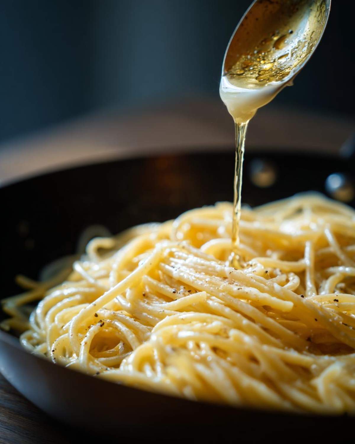 Alfredo sauce being poured from a spoon onto a pan of spaghetti, creating a creamy, delicious dish.