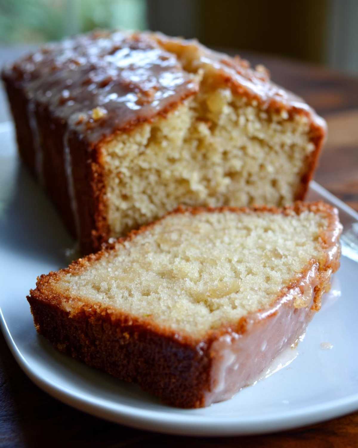 A slice of glazed Amish applesauce cake on a white plate, with the rest of the loaf in the background.