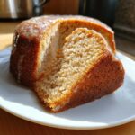 A slice of glazed Amish applesauce cake on a white plate, showcasing the cake's texture and moistness.