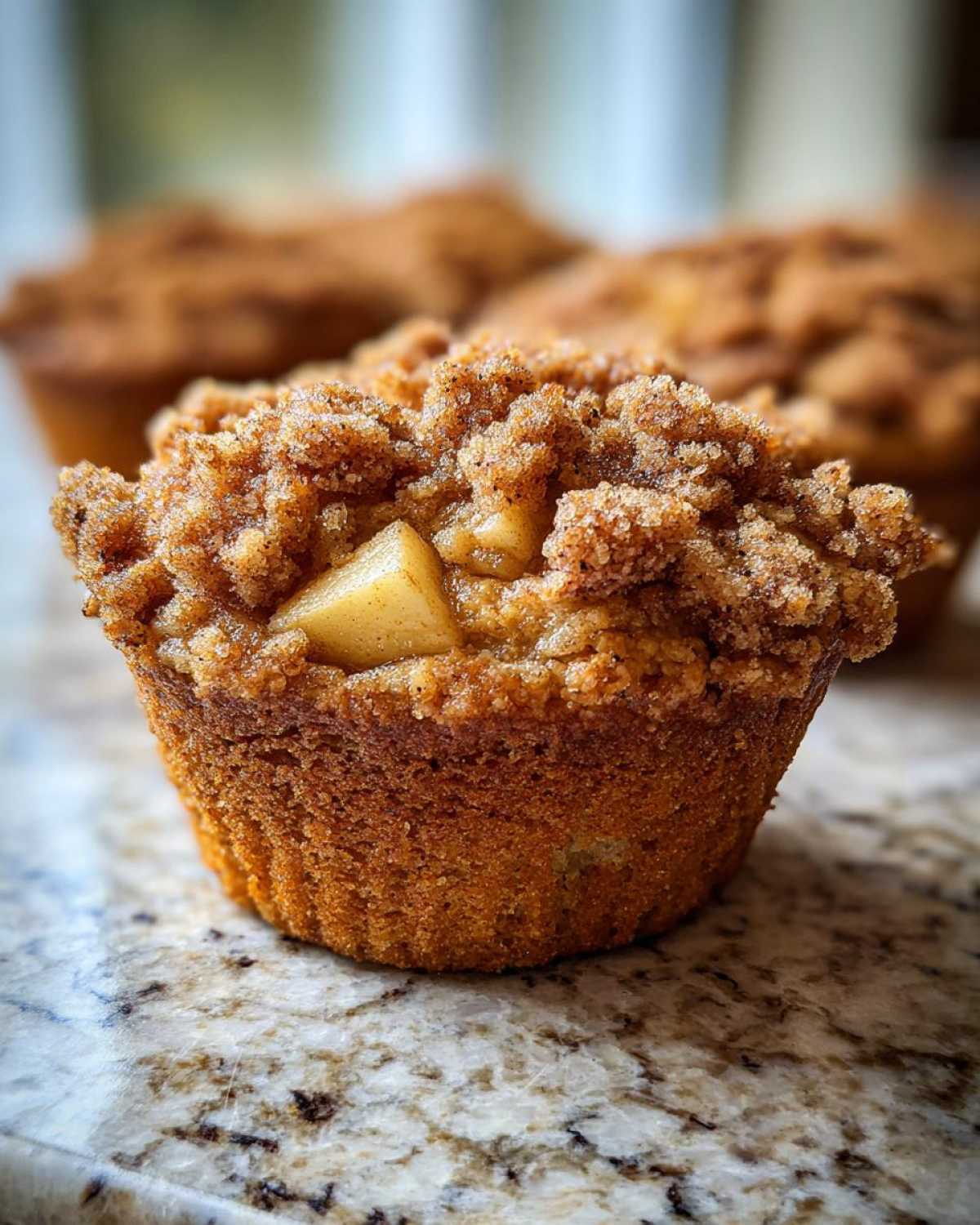 A close-up of an apple oatmeal muffin with a crumble topping and a visible apple piece.