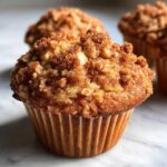 Close-up of a freshly baked apple oatmeal muffin with a cinnamon crumble topping.