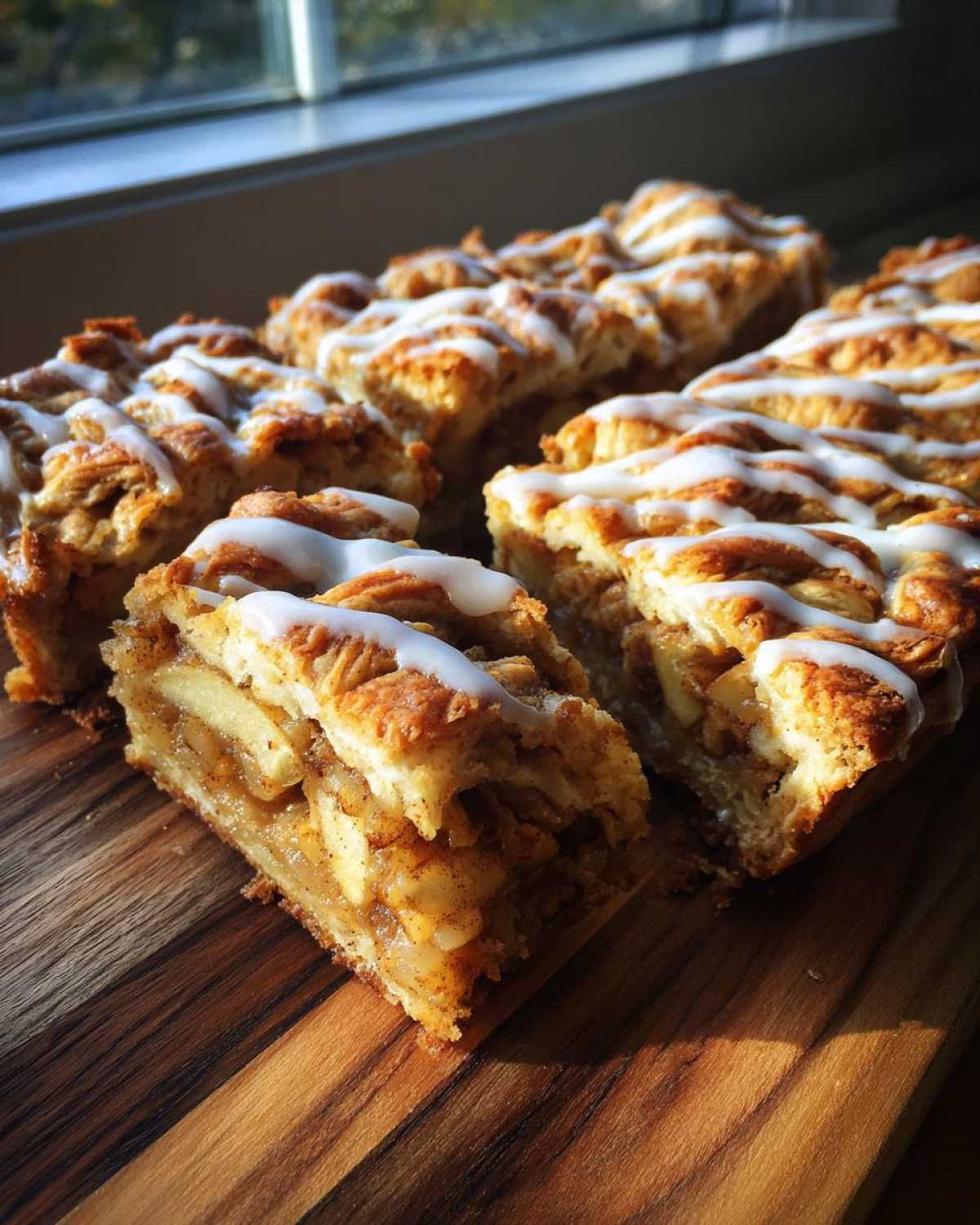 Close-up of apple slice bars drizzled with white icing on a wooden board, ready to be served.