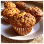 A plate of freshly baked banana muffins, showcasing their golden-brown tops and paper liners.