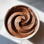 Overhead view of a bowl filled with rich, swirled chocolate frosting.