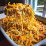 A spoonful of creamy chicken spaghetti casserole being lifted from a baking dish, showing melted cheese and spaghetti.
