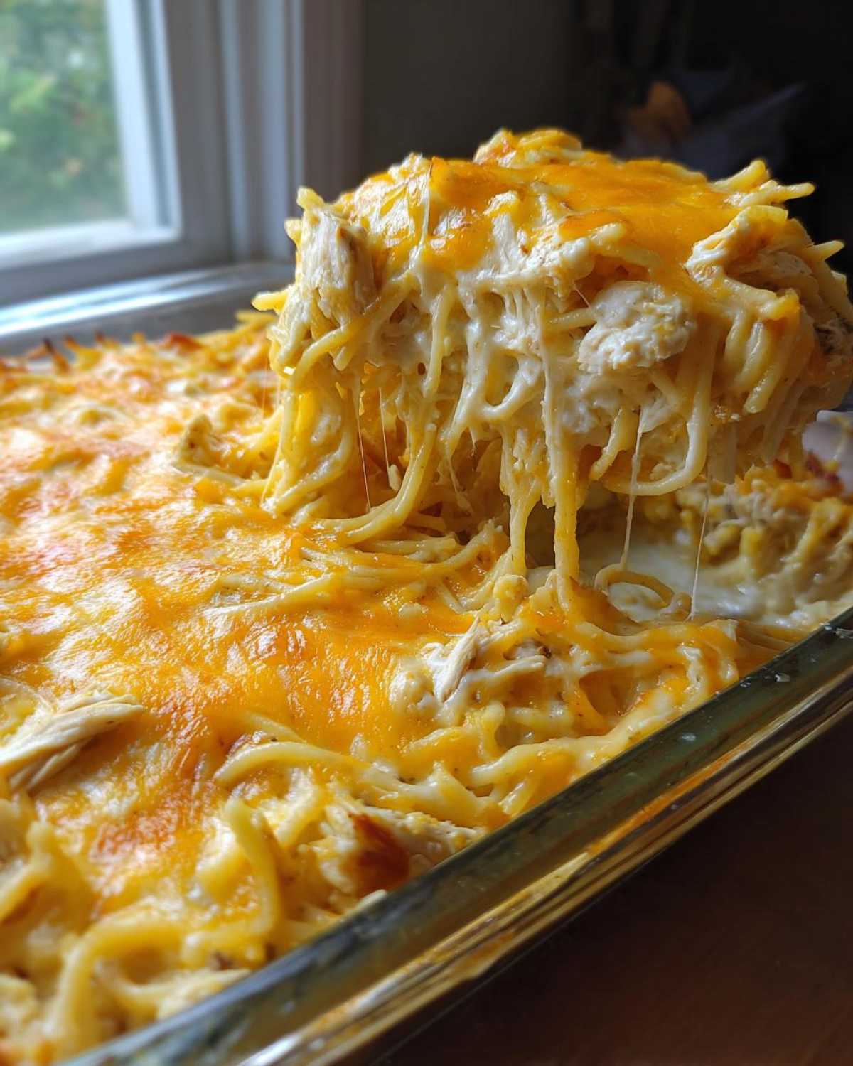 A spoonful of cheesy chicken spaghetti casserole lifted from a glass baking dish, showing the creamy texture and melted cheese.