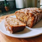 A delicious cinnamon apple cake loaf with icing and a slice cut out, showing the apple pieces inside.