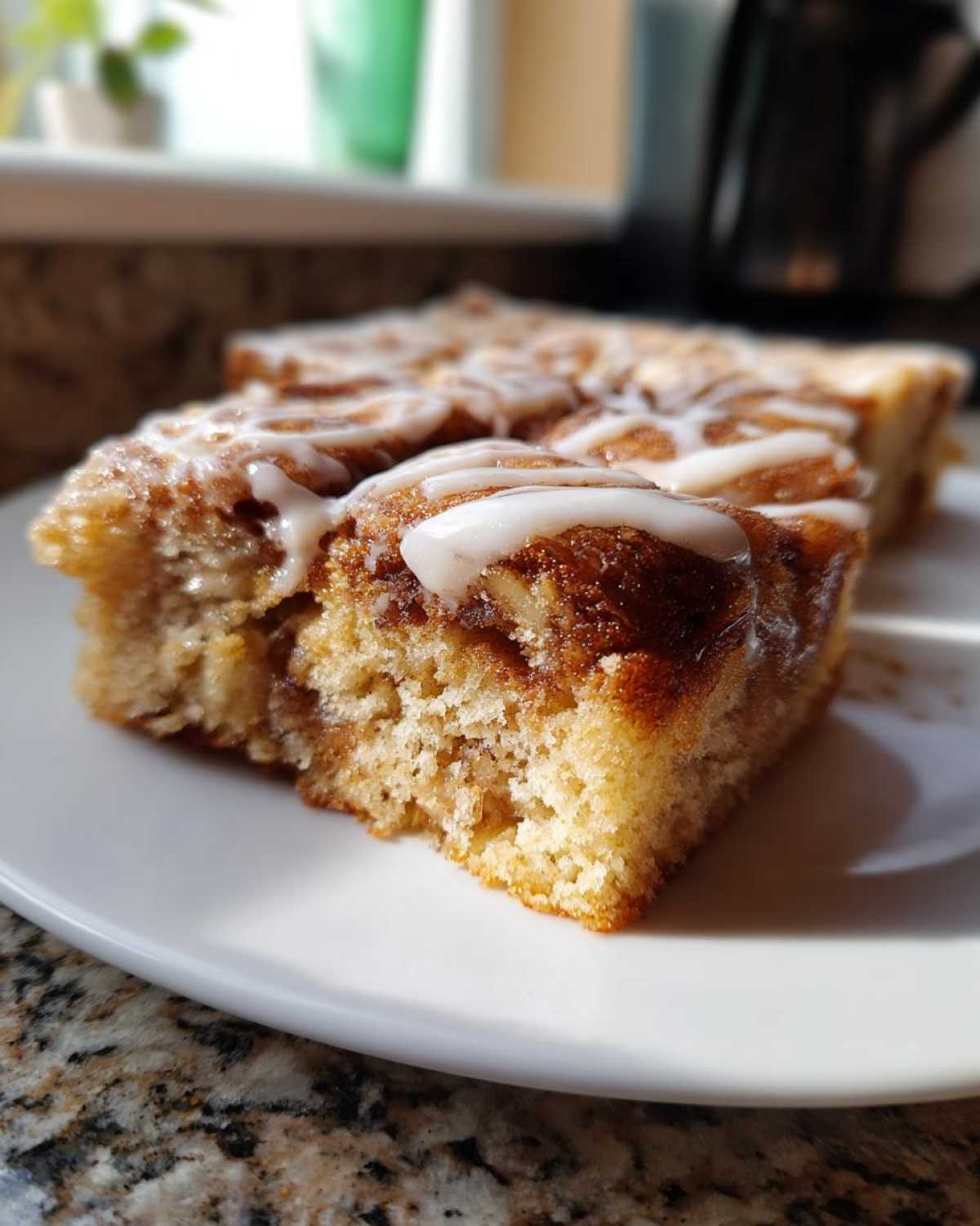 Close-up of a slice of cinnamon apple cake with a sweet glaze on a white plate.