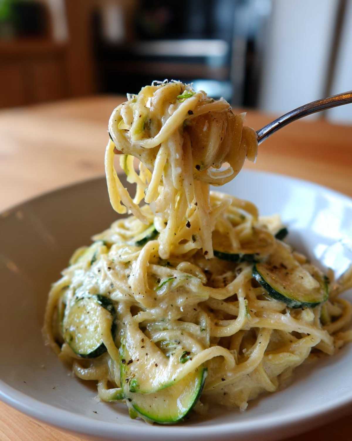 A fork lifting a portion of creamy zucchini pasta, showcasing the dish's texture and sauce.
