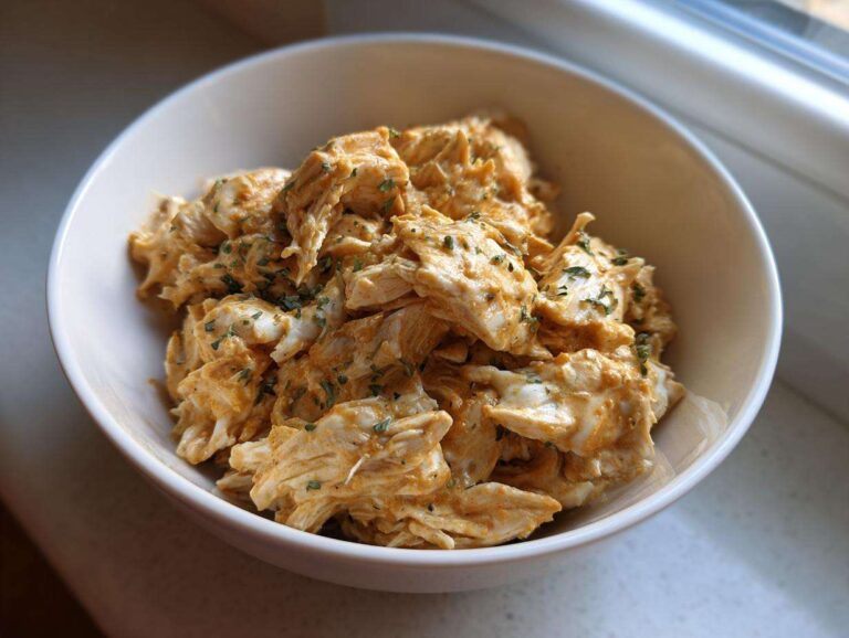 A bowl filled with shredded crock pot ranch chicken, seasoned with herbs, ready to eat.