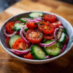 Close-up of a vibrant cucumber tomato salad with red onion in a blue and white bowl.