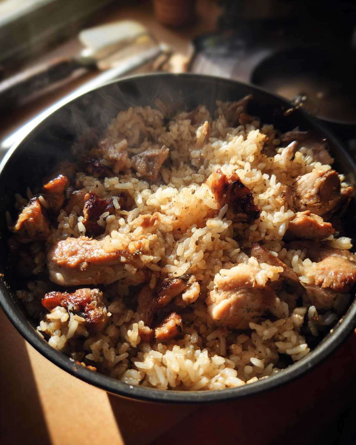 A steaming pot of freshly cooked garlic chicken rice, showcasing tender chicken pieces mixed with fluffy rice.