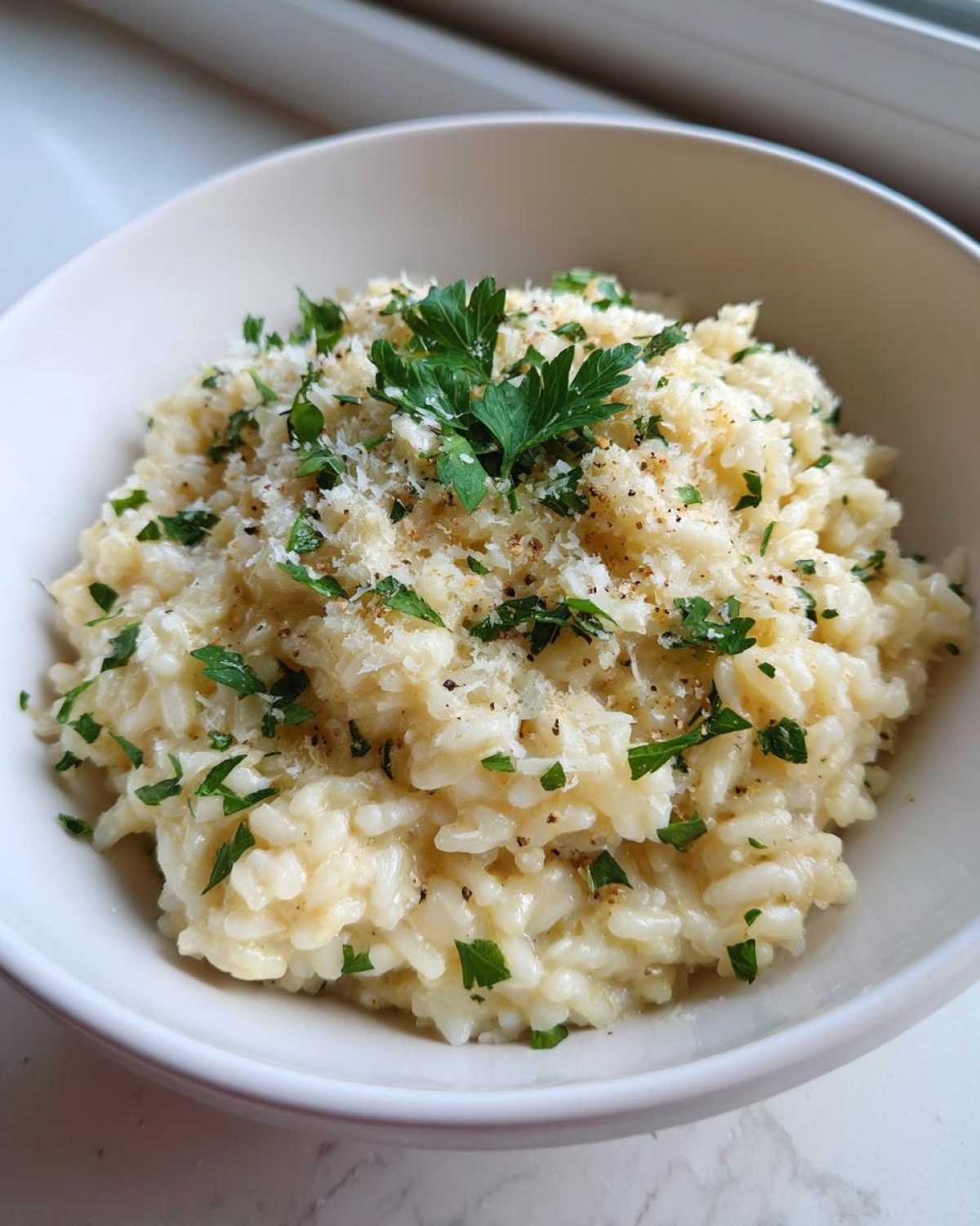 A bowl of creamy garlic parmesan risotto, garnished with fresh parsley and grated parmesan cheese.