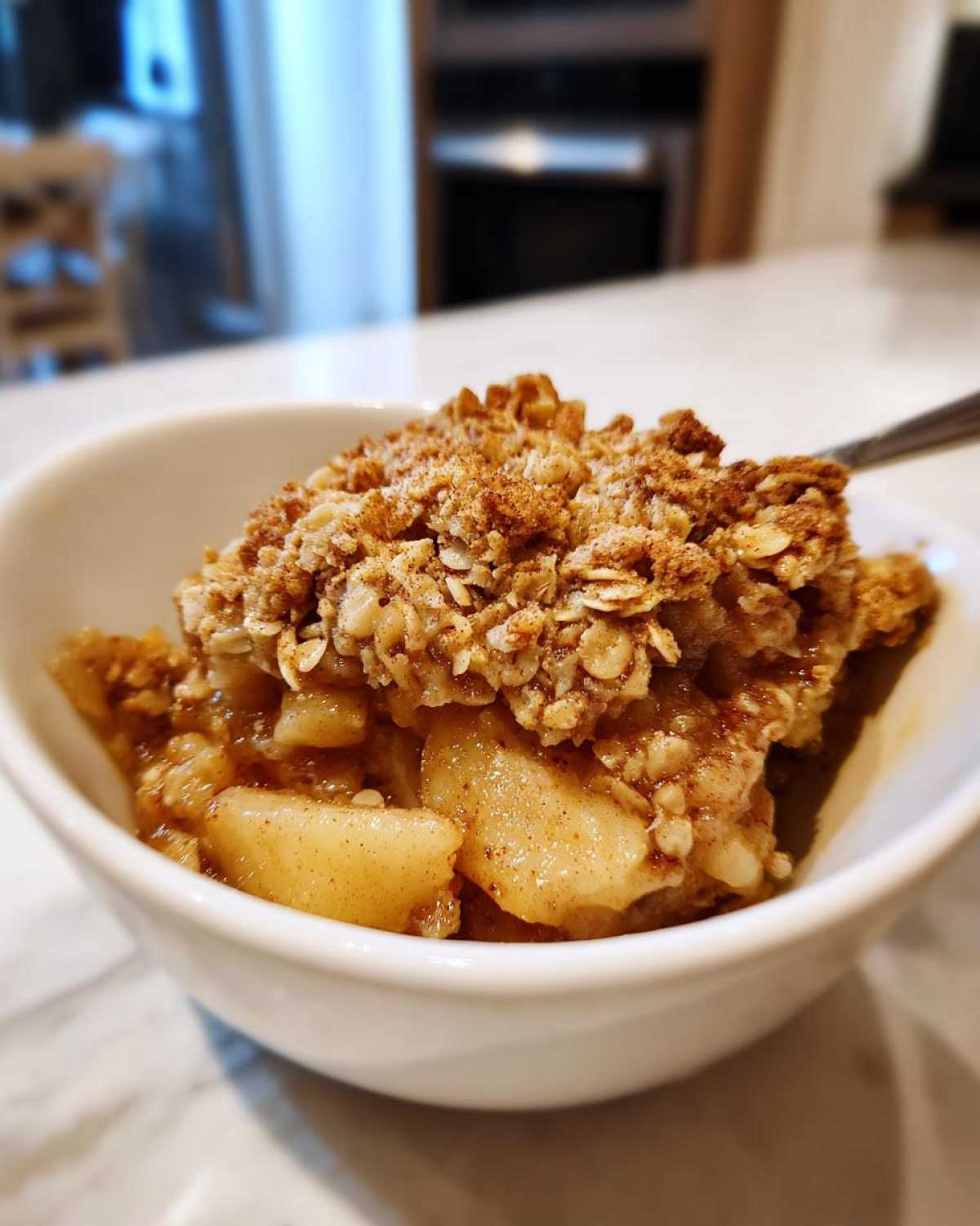A bowl of healthy apple crisp with cooked apples and a crunchy oat topping, ready to eat.