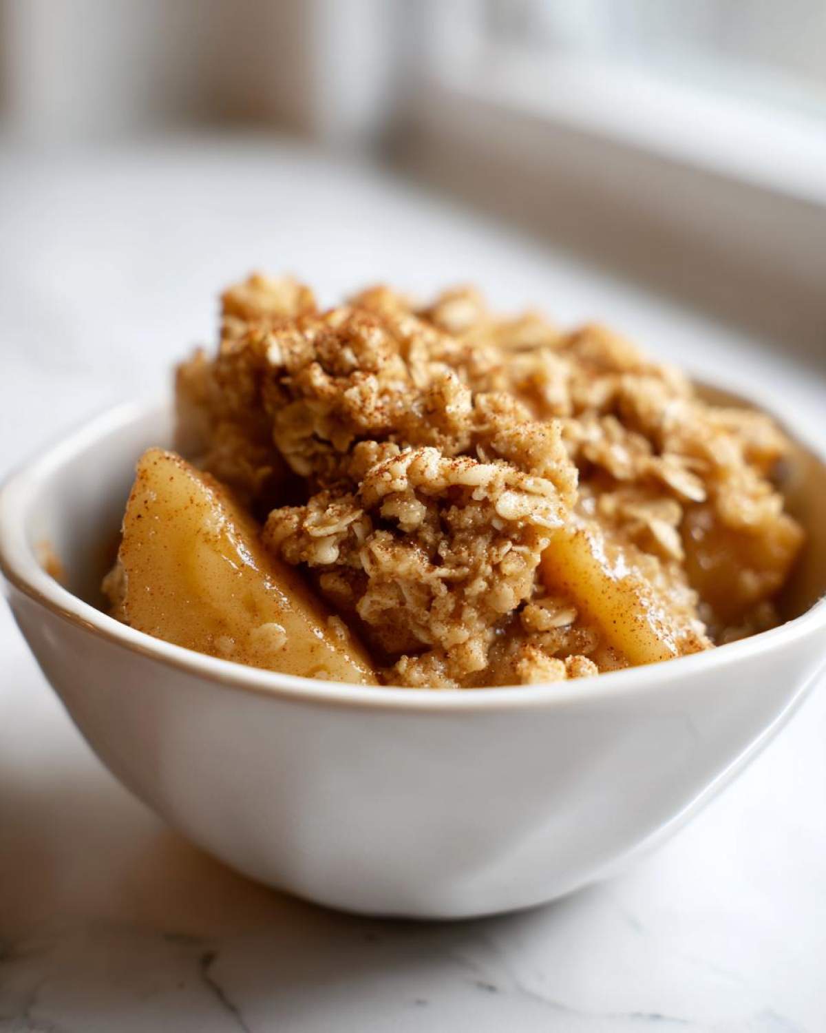 Close-up of a bowl filled with healthy apple crisp, featuring baked apples and an oat-based crumble topping.
